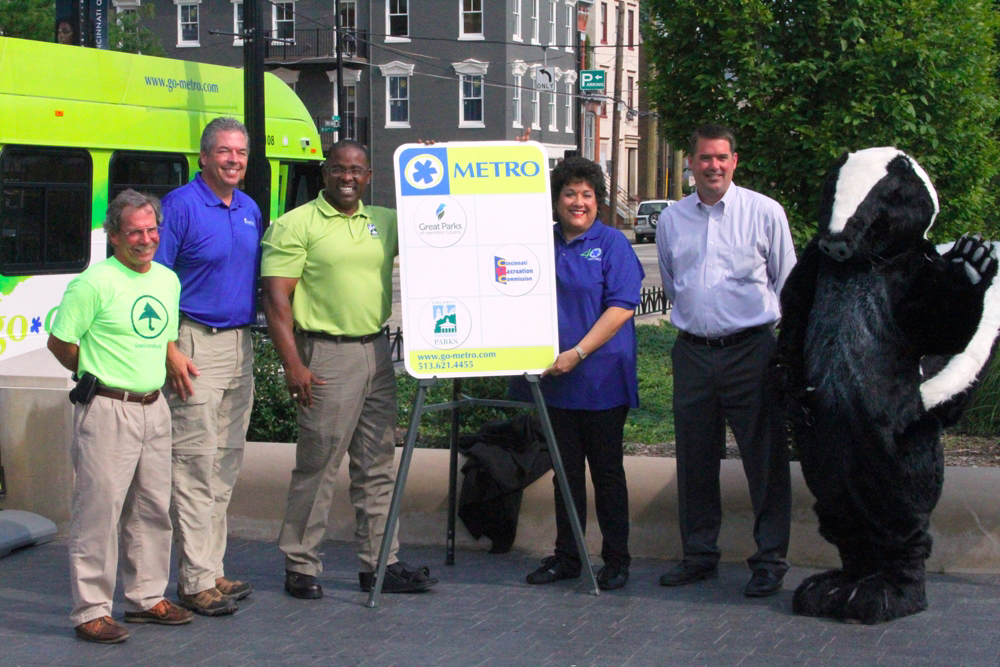 , Left to Right: Green Umbrella Executive Director Brewster Rhoads, Great Parks of Hamilton County Executive Director Jack Sutton, Cincinnati Parks Director Willie F. Carden Jr., Metro CEO Terry Garcia Crews, CRC Recreation Director Christopher Bigham and the Cincinnati Parks skunk critter helped unveil the new parks bus stop sign on July 10 in Cincinnati's Washington Park.