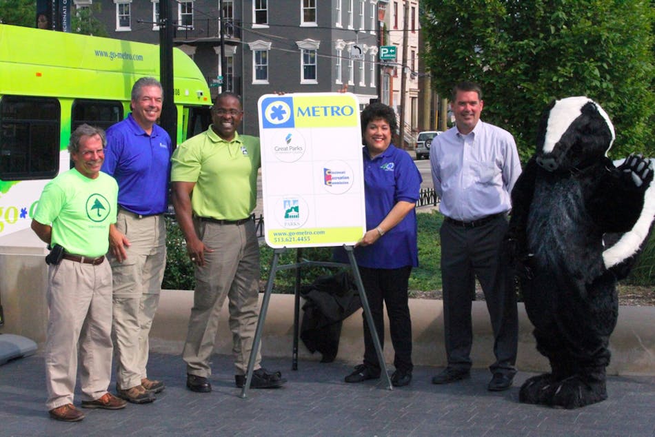 , Left to Right: Green Umbrella Executive Director Brewster Rhoads, Great Parks of Hamilton County Executive Director Jack Sutton, Cincinnati Parks Director Willie F. Carden Jr., Metro CEO Terry Garcia Crews, CRC Recreation Director Christopher Bigham and the Cincinnati Parks skunk critter helped unveil the new parks bus stop sign on July 10 in Cincinnati&apos;s Washington Park.
