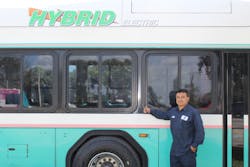 Willy Acuna, maintenance technicians poses in front of hybrid buses. Willy Acuna, maintenance technicians poses in front of hybrid buses.