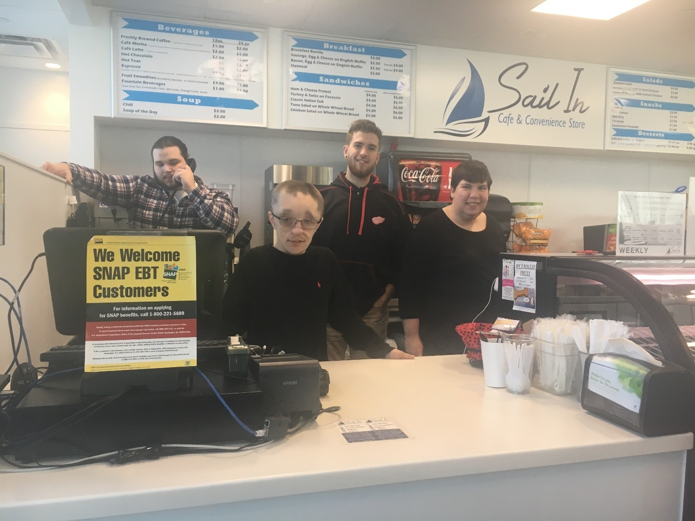 Sail In students and staff pose behind the counter at the Sail In Caf&eacute;. From left to right: Josh Feher (Sail In employee), David Kemske (student), Kyle Duffy (Community Enterprises job trainer), and Kim London (student).