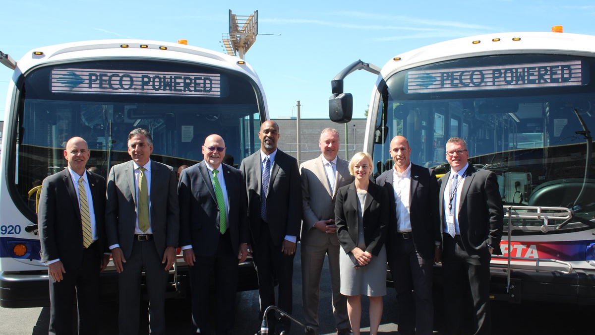 SEPTA officials and industry partners stand in front of two of the transit authority's new battery electric buses at the Southern Bus Depot.