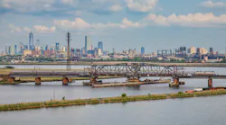 An Amtrak train crosses the Portal North Bridge with New York City in the background.