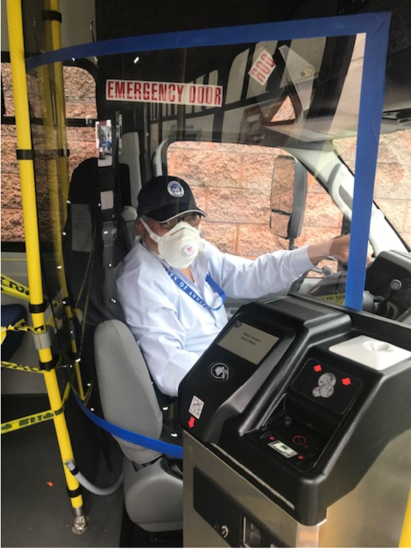 A bus operator sits behind the plexiglass barrier, outlines in blue tape.