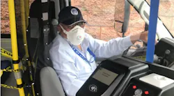 A bus operator sits behind the plexiglass barrier, outlines in blue tape.