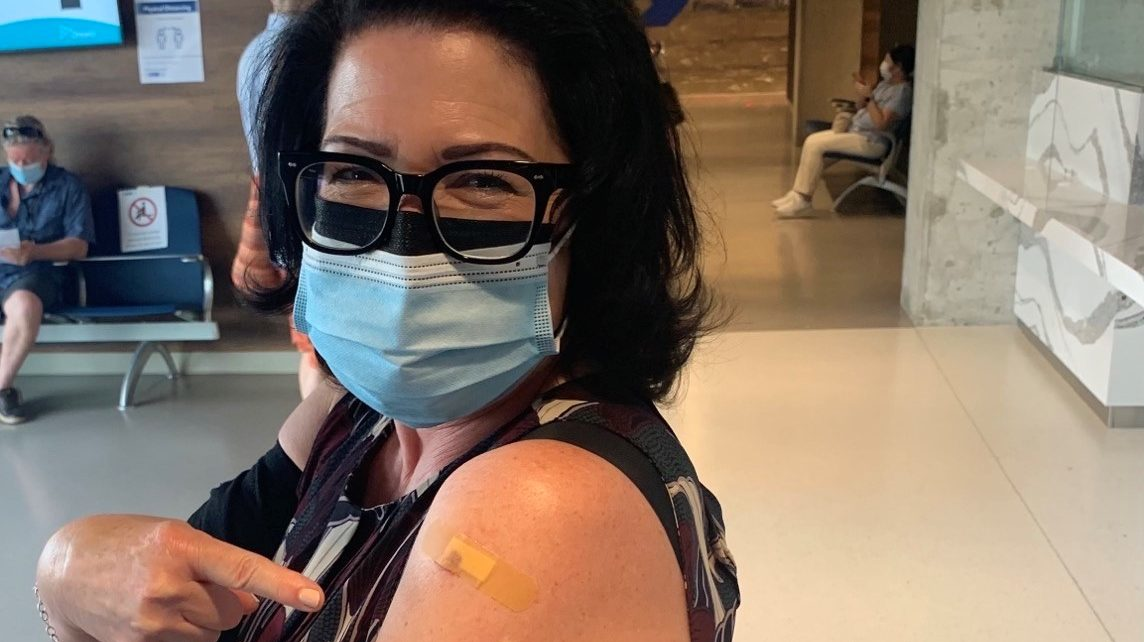 Anne Marie Aikins, head of media and public relations, proudly shows proof of her COVID-19 jab.