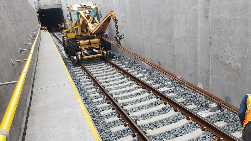 In this July 2021 photo, crews lay third rail by the track for the yard lead tunnel approach structure in Harold Interlocking.