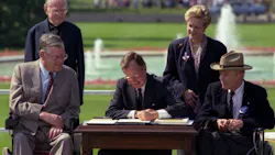 President George Bush signs into law the Americans with Disabilities Act of 1990 on the South Lawn of the White House. L to R, sitting: Evan Kemp, Chairman, Equal Employment Opportunity Commission, Justin Dart, Chairman, President's Committee on Employment of People with Disabilities. L to R, standing: Rev. Harold Wilke and Swift Parrino, Chairperson, National Council on Disability, 07/26/1990.
