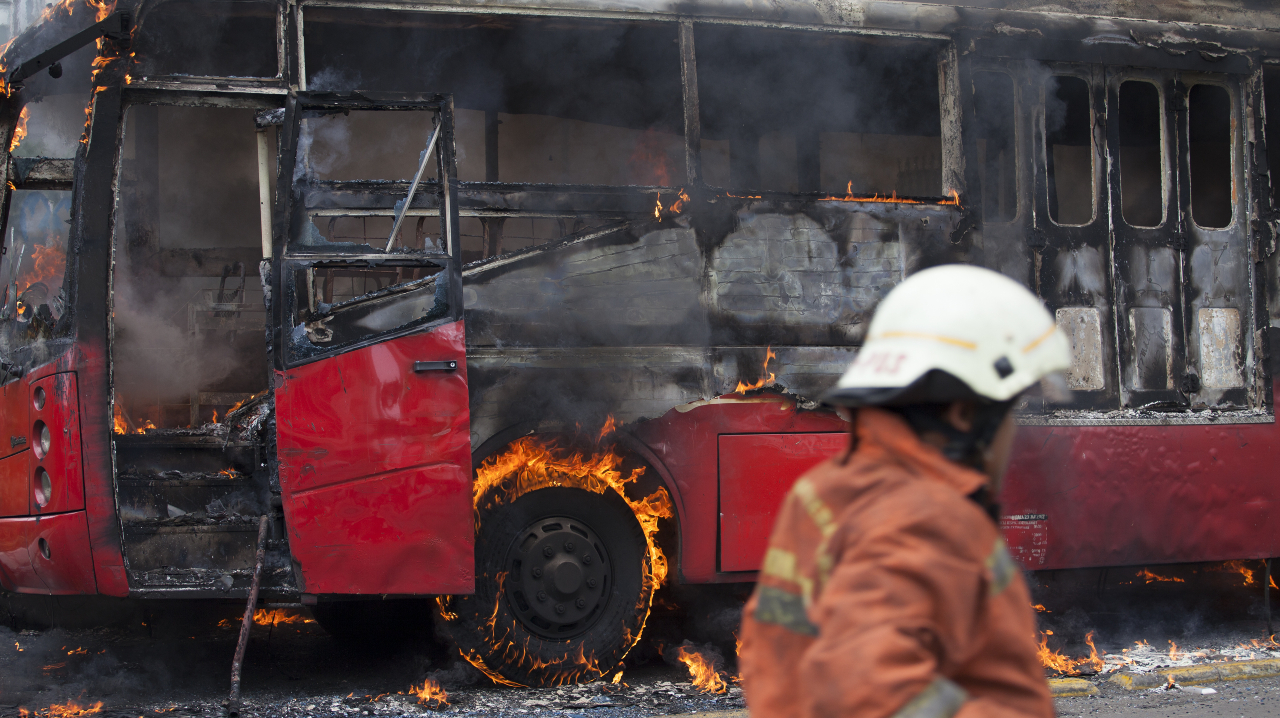 A bus burning from a fire with fire department on site.