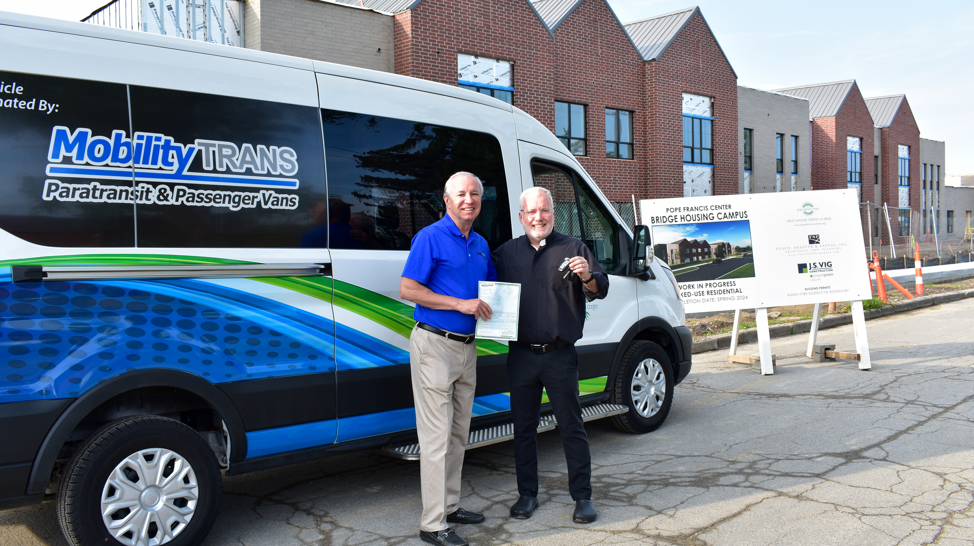 Dave Brown, general manager of MobilityTRANS, hands over the title and keys of a brand new Ford E-Transit to Fr. Tim McCabe, executive director of the Pope Francis Center.