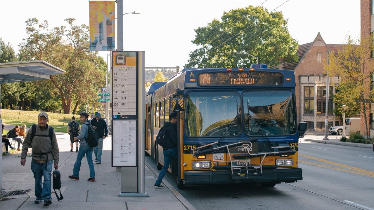 People board a route 70 bus in the U District on a sunny afternoon.
