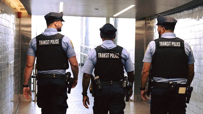 three SEPTA transit police officers walk with backs to camera at train station