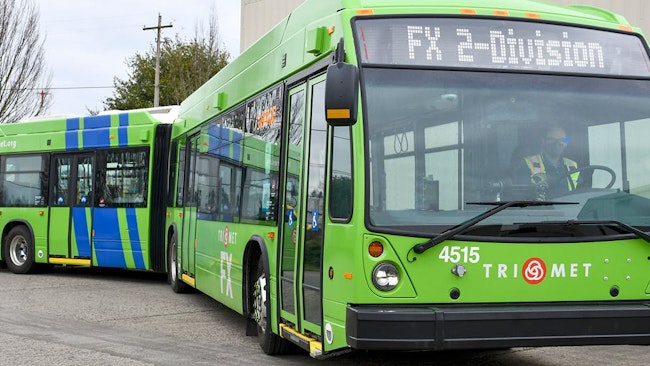 A green 60-foot TriMet bus drives down a street