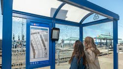 two women stand with back to camera looking at ePaper display in blue bus shelter two women stand with back to camera looking at ePaper display in blue bus shelter