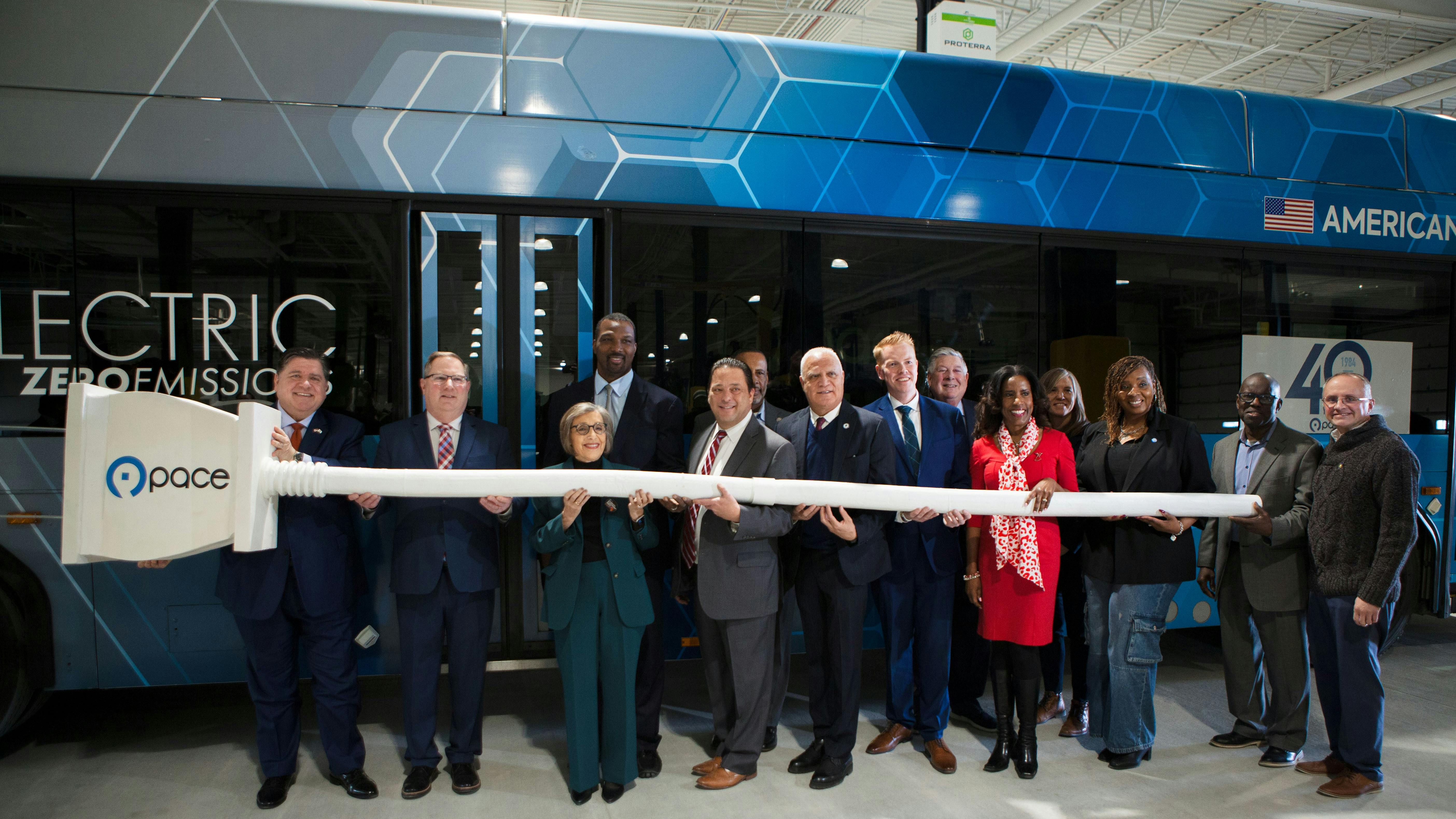 officials stand with giant plug in in front of Pace electric bus