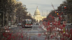 bus drives down road in D.C. with capitol building behind bus drives down road in D.C. with capitol building behind