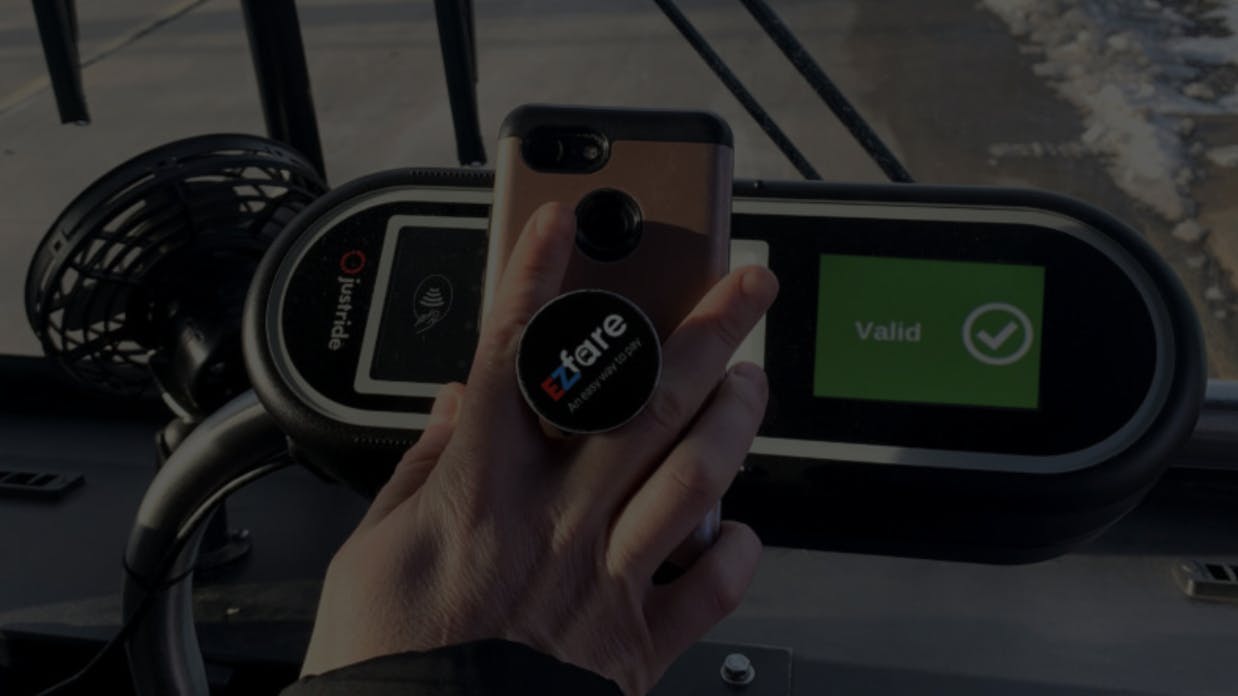 person holds mobile device over fare validator on bus