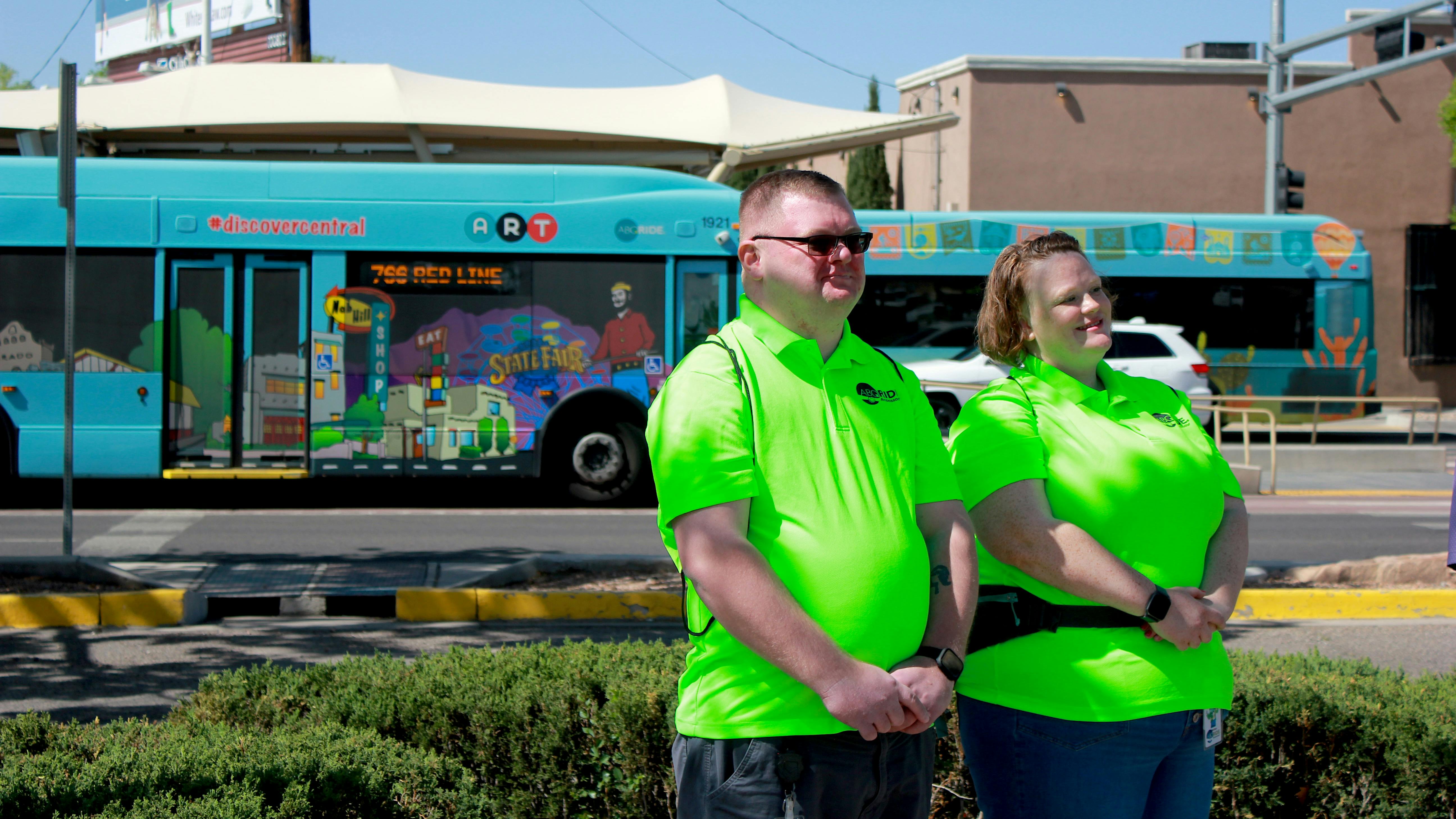 two ABQ Ride ambassadors in neon green shirts pose in front of a bus