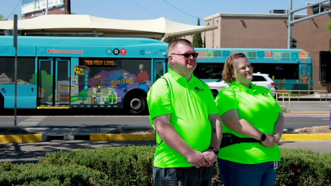 two ABQ Ride ambassadors in neon green shirts pose in front of a bus