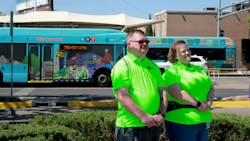 two ABQ Ride ambassadors in neon green shirts pose in front of a bus two ABQ Ride ambassadors in neon green shirts pose in front of a bus