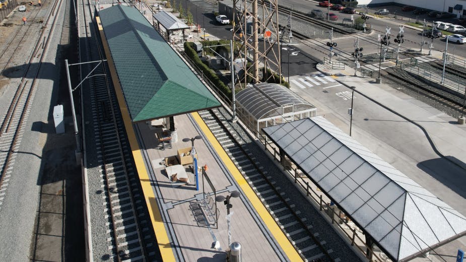 empty rail station platform in between two sets of tracks with a forest green canopy