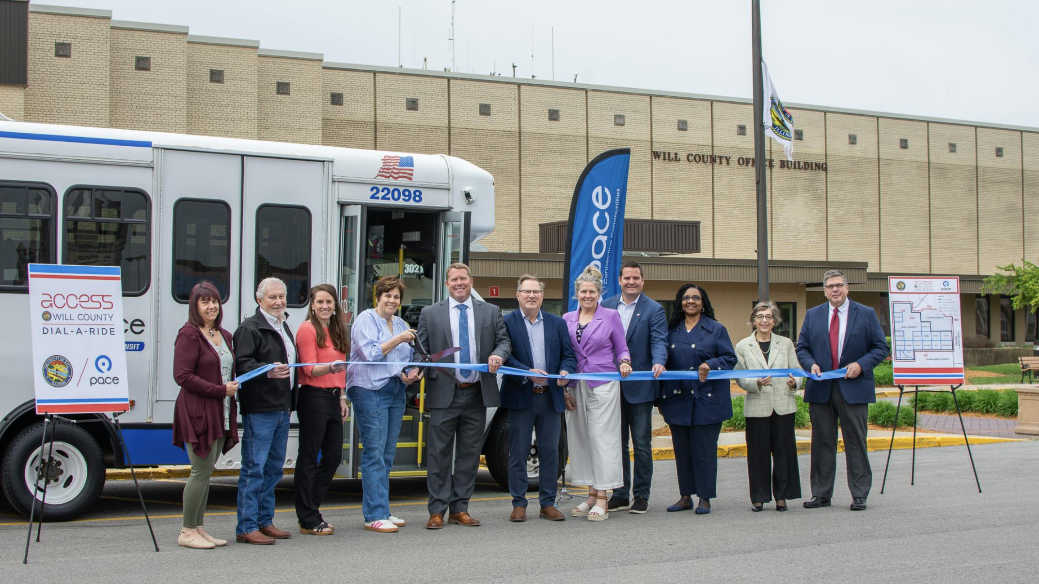 county and pace officials stand in a line in front of a pace cutaway bus to cut a ribbon