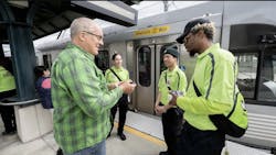 L.A. Metro transit ambassadors dressed in neon green shirts interact with a rider at a rail platform L.A. Metro transit ambassadors dressed in neon green shirts interact with a rider at a rail platform