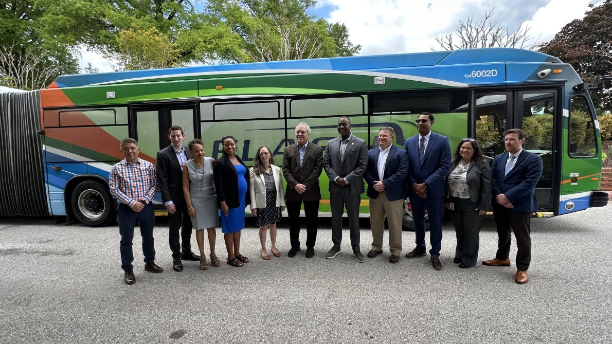 line of people stand in front of parked articulated bus