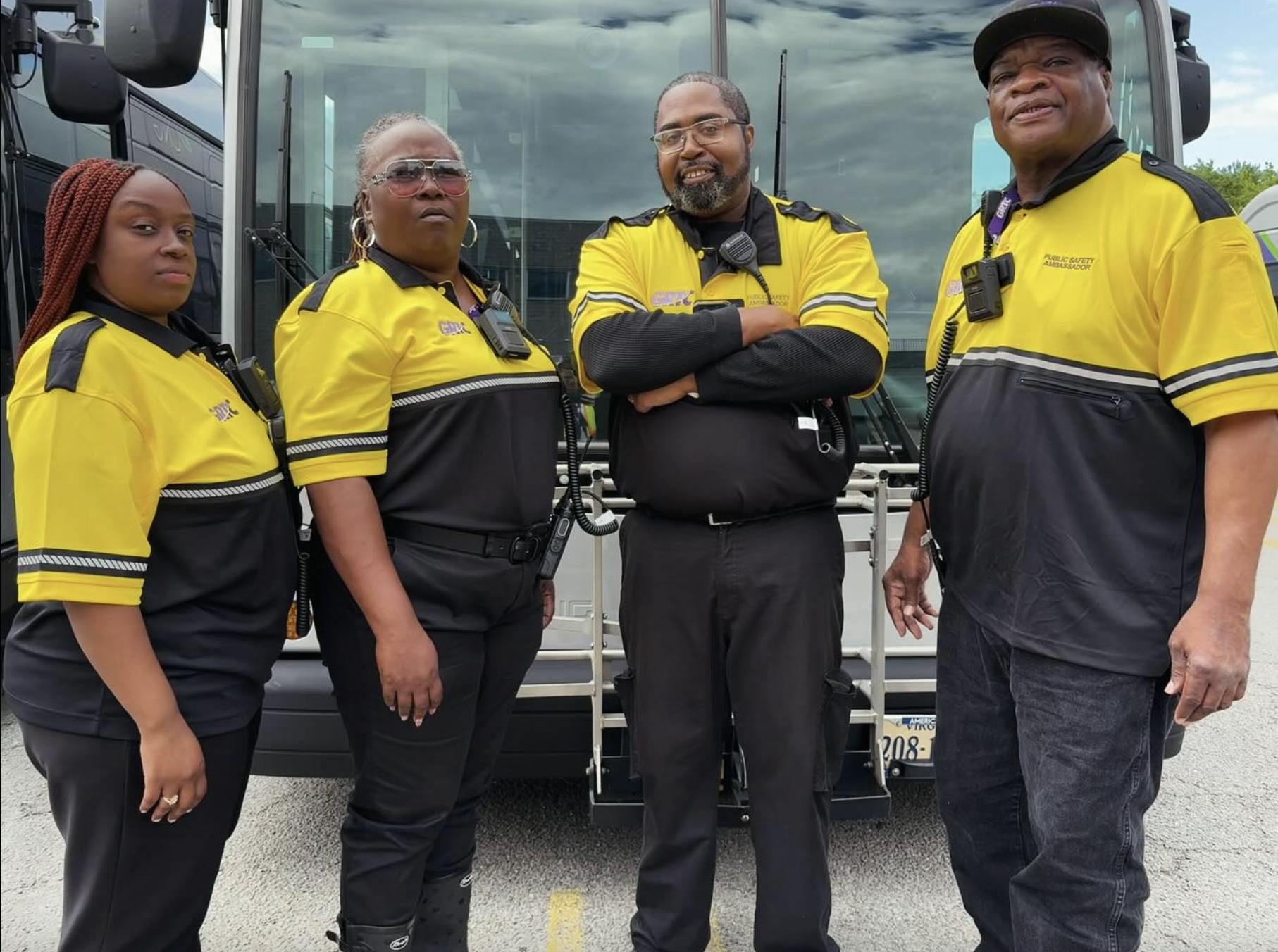 four public safety ambassadors in black and yellow uniform stand in front of GRTC bus