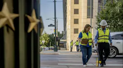 two people in safety vests and work hats mark pavement in downtown Austin