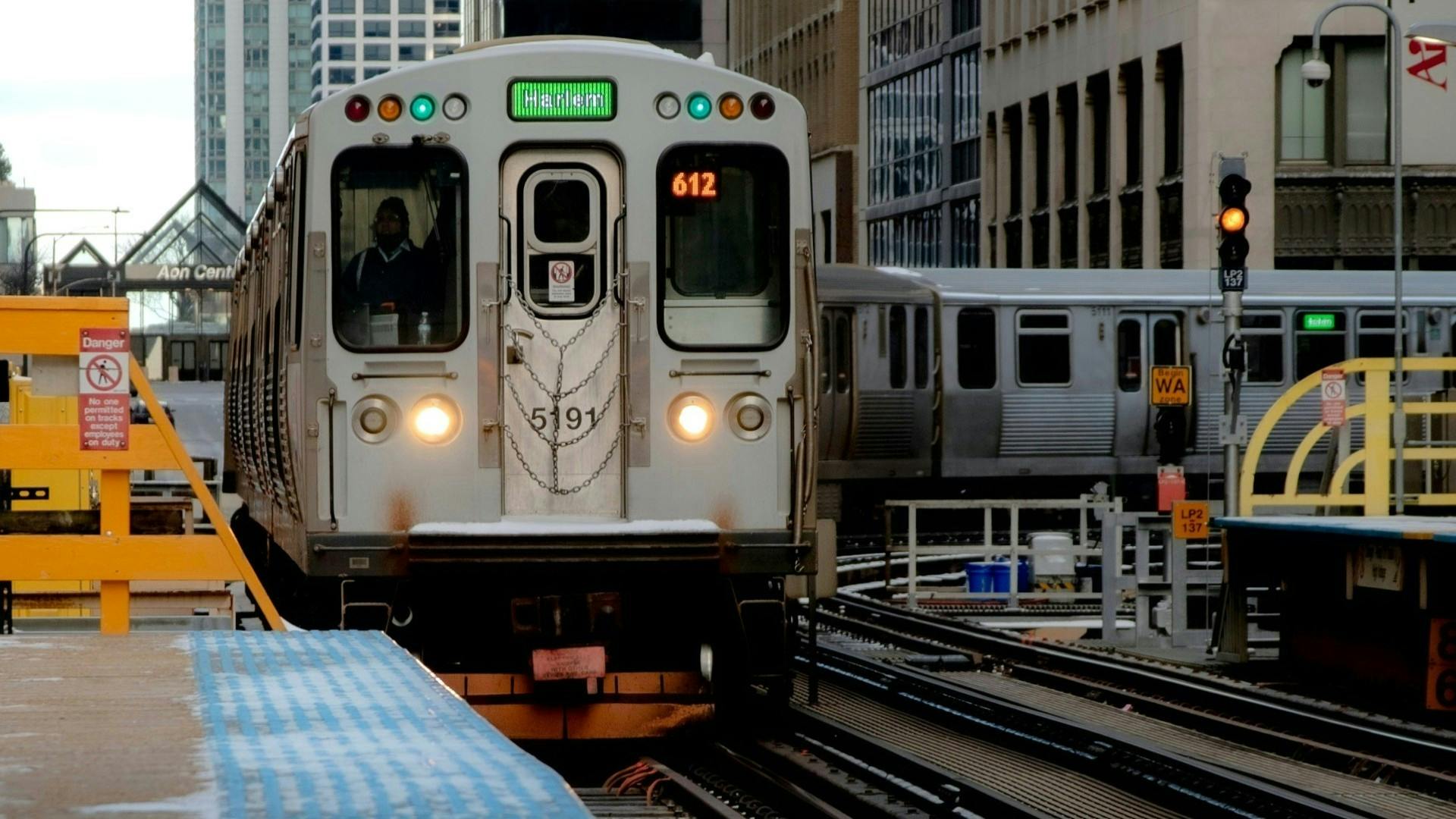 Chicago Transit Authority train approaches a passenger platform after a tight curve. A sign warns of the danger of trespass onto the tracks.