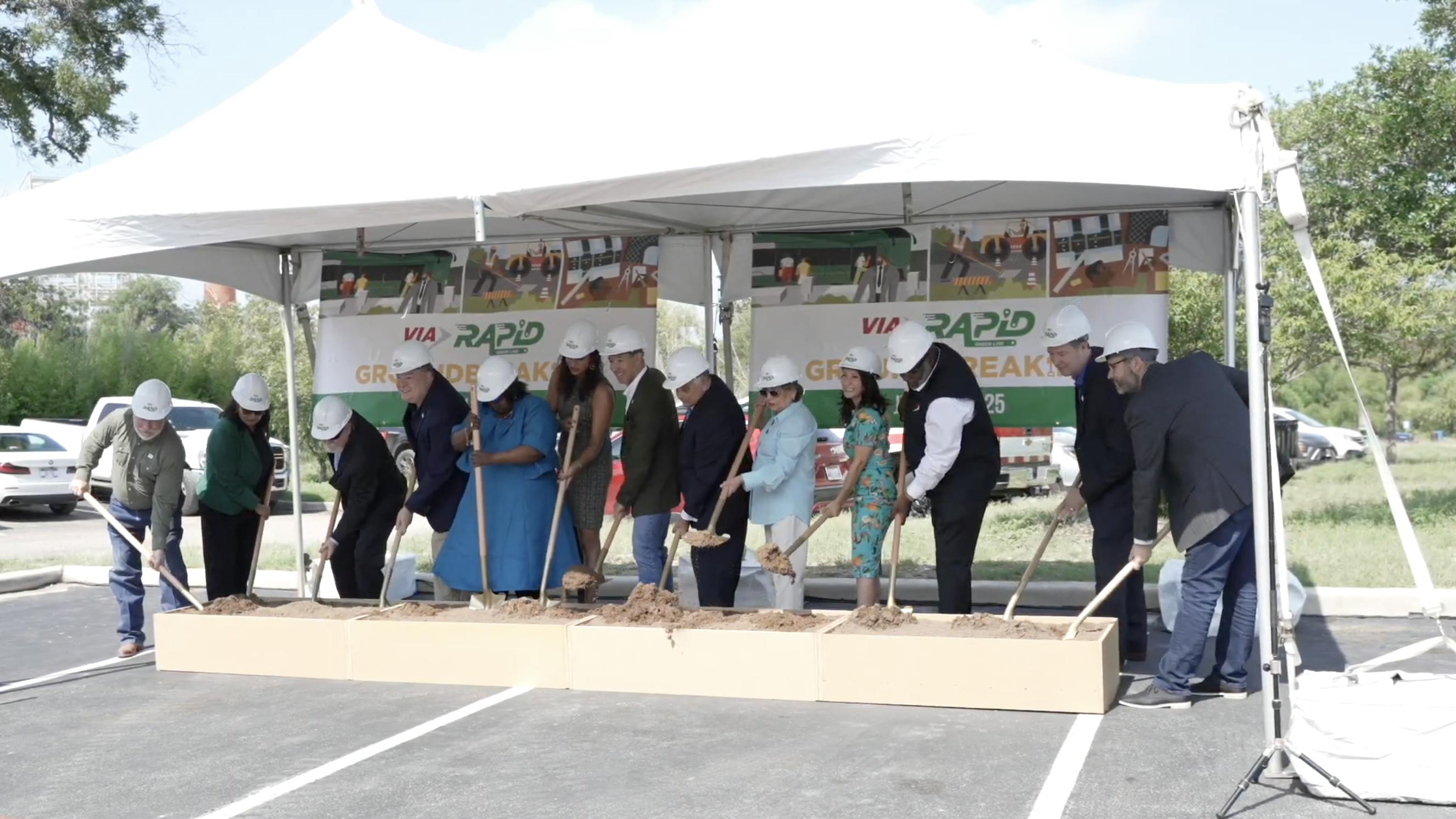stakeholders stand in a line in front of a VIA Green Line banner and dig shovels into a box of dirt