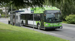White and green BC Transit wrapped bus pulls over at a bus stop with a shelter and bench
