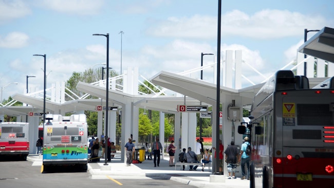 three buses pull into a transit center at bus bays with people lined up on a platform
