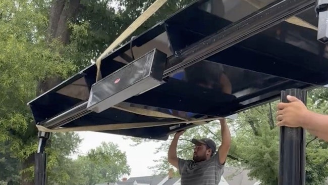 man holds up roof of bus shelter during installation