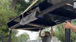 man holds up roof of bus shelter during installation