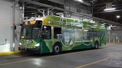 An electric NJ Transit bus sits parked with its lights on bearing 'it's electric' livery. An electric NJ Transit bus sits parked with its lights on bearing 'it's electric' livery.