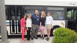 a group of people stand posing in front of a bus outside a group of people stand posing in front of a bus outside