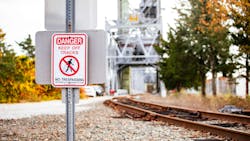 Keep Off Tracks Warning. A warning sign reading Danger Keep Off Tracks stands beside a railway, with autumn trees and the Cape Cod Canal Railroad Bridge in the background. Keep Off Tracks Warning. A warning sign reading Danger Keep Off Tracks stands beside a railway, with autumn trees and the Cape Cod Canal Railroad Bridge in the background.