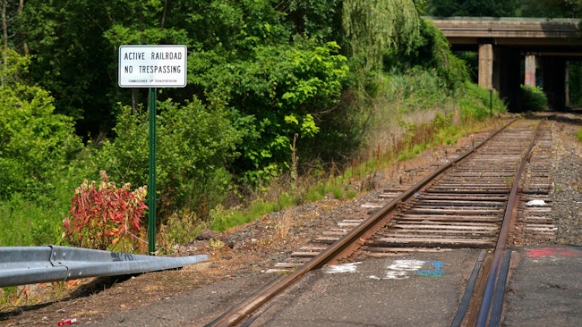 at-grade empty railroad crossing with sign that says no trespassing active railroad next to it