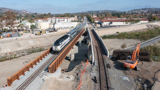 A drone shot of the new and old bridge standing next to each other with a train passing over the new bridge.