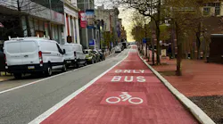 The image shows a long shot of a new red-painted bus lane.