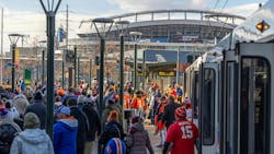 The image shows riders filtering off of public transit at a large event. The image shows riders filtering off of public transit at a large event.