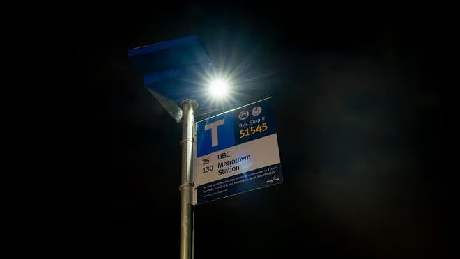 A solar light is shown mounted atop a bus stop pole.