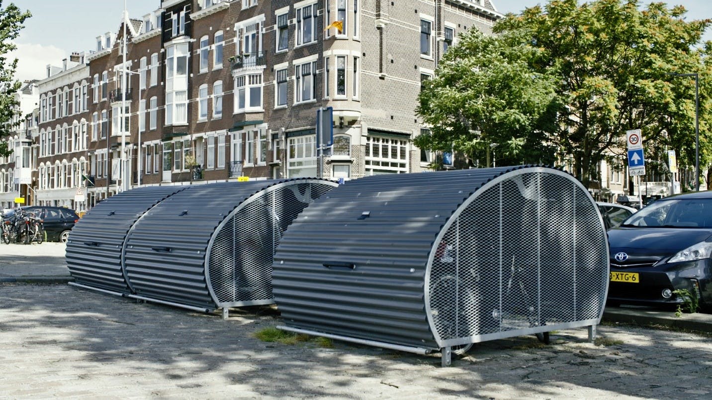 Bike storage sheds are spread out in front of parking spaces.