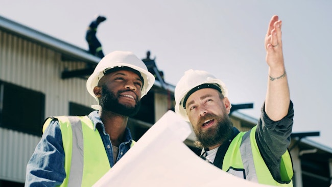 Construction workers talk over plans and point at a construction site.