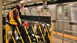 The image shows two construction workers working on an MTA subway. The image shows two construction workers working on an MTA subway.