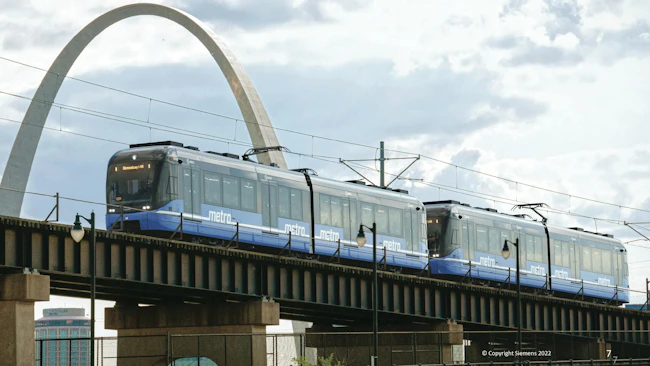 The image displays a rendering of the future LRVs on a track in front of the Arch.