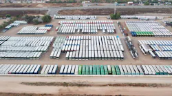 The image shows a drone shot of a lot full of buses.