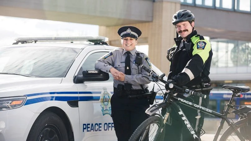 Transit peace officers stand posed in front of a patrol car and bike.