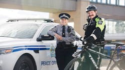 Transit peace officers stand posed in front of a patrol car and bike. Transit peace officers stand posed in front of a patrol car and bike.